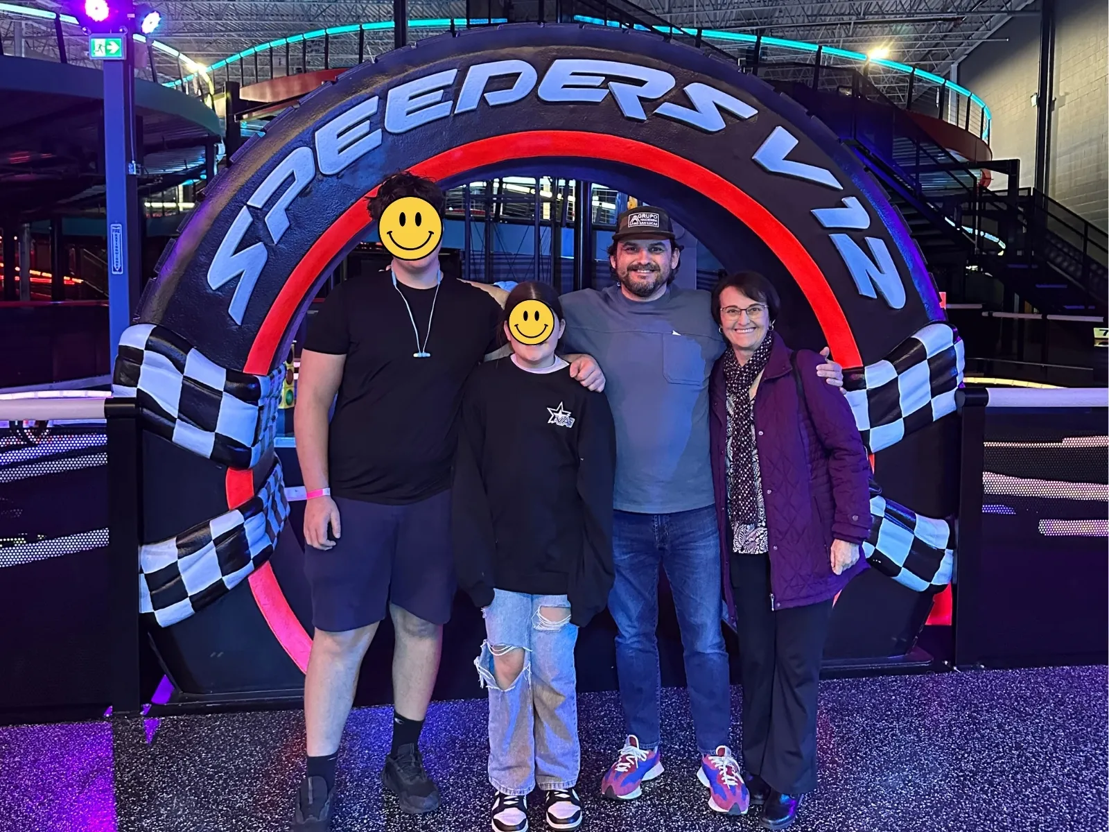Me with the kids and family under the neon SPEEDERS V12 arch at a go-kart track.